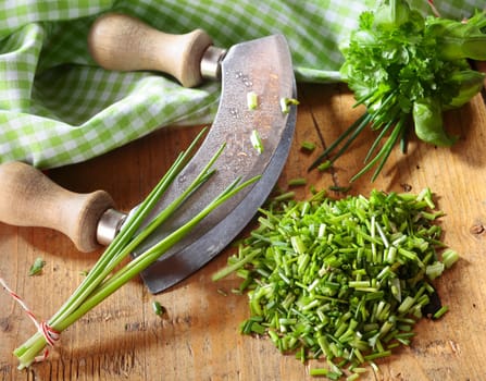 High angle view of a curved kitchen rocker blade used for chopping a pile fresh chives for use as an ingredient in cooking and salads