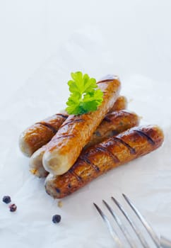 Four cooked sausages on a plate with a sprig of parsley and prongs of a fork.