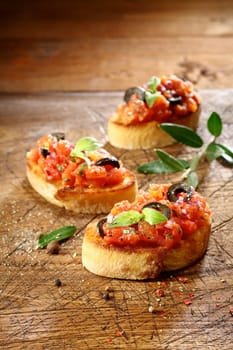 Preparing vegetable bruschetta with finely chopped tomato, onion and seasonings served on slices of crisp golden crusty toasted baguette on a grungy old wooden surface with copyspace