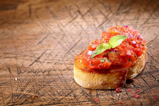 Tasty bruschetta appetizer or antipasti of chopped seasoned ripe red tomatoes and onion garnished with basil on crisp toasted baguette lying on a grunge wooden surface with copyspace