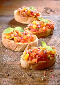 Preparing tasty Italian bruschetta, a small appetizer on toasted crisp crusty bread, with several prepared tomato bruschetta on an old wooden chopping board with scattered seasoning