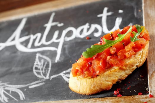Tasty tomato bruschetta garnished with rocket leaves on a small slate blackboard with a handwritten antipasti sign