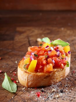 Tomato bruschetta or antipasti with a finely chopeed tomato and onion mixed with oil on a slice of crisp crusty toasted baguette surrounded by a scattering of spices on a wooden surface with copyspace