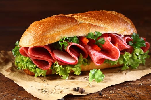 Freshly baked golden crusty baguette filled with fresh lettuce and thinly sliced salami seasoned with spices on crumpled brown paper