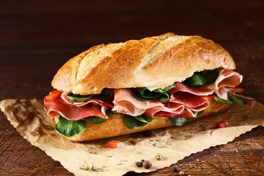 Preparing a delicious ham and fresh basil baguette on a sheet of grungy oily paper with remnants of seasoning