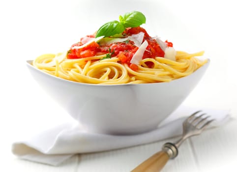 Pasta in a white bowl with tomato sauce and fresh basil set against a white napkin on a white table.