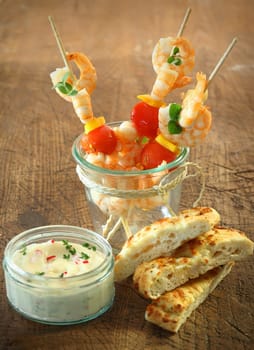 Tasty appetizers of seafood cocktail sticks with shrimps, cheese and tomato standing in a jar alongside fresh focaccia bread and a tub of tartare sauce