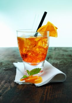 Colourful glass of rum and orange cocktail garnished with fresh fruit, rind and mint leaves standing on an old wooden bar counter