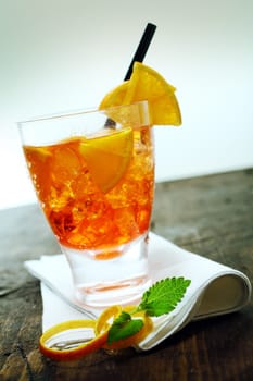Glass of colourful rum cocktail with fresh orange pieces and ice served on a napkin with mint and orange rind at a bar or restaurant