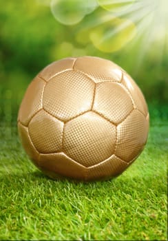 Conceptual image of a healthy outdoor lifestyle playing soccer in summer with a gold coloured soccer ball standing on lush green grass under the rays of the sun