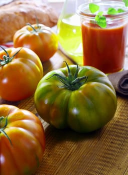 Unripe green ribbed tomato on a kitchen table with other ripe red tomatoes for use in preparing fresh tomato paste as an ingredient in Italian cooking