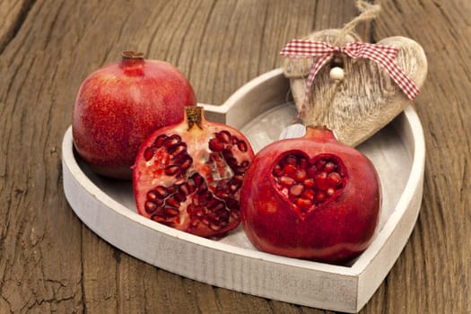 Whole,half and one heart-shaped pomegranate on a heart-shaped wooden tray