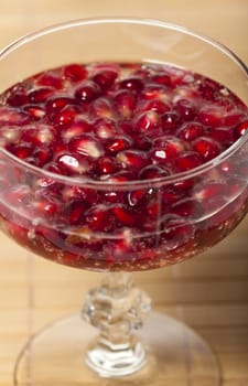 Pomegranate seeds in a champagne glass filled with sparkling wine on a bamboo mat