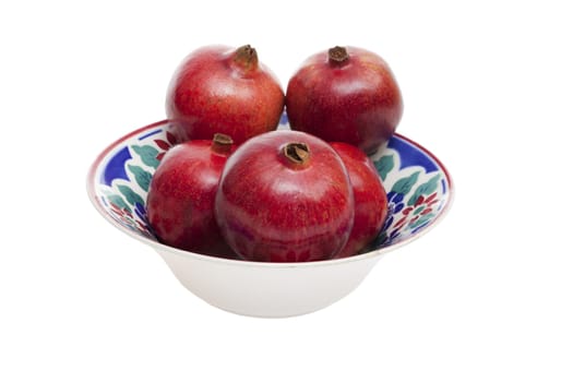 Five ripe pomegranates in a colorful old porcelain bowl against a white background
