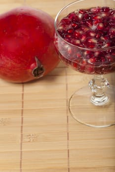Pomegranate seeds in a champagne glass filled with sparkling wine on a bamboo mat