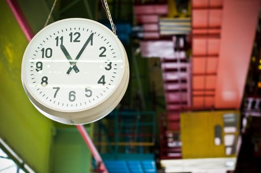 big clock hanging down from factory ceiling