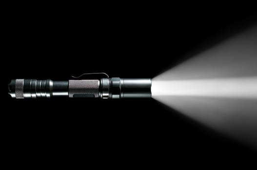 tactical police and military flashlight on black background with visible beam of light