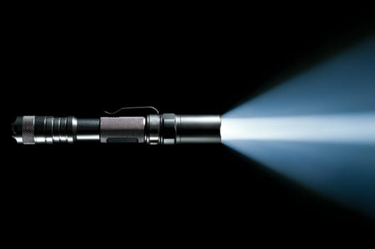 tactical police and military flashlight on black background with visible beam of light