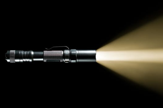 tactical police and military flashlight on black background with visible beam of light