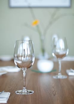 two empty glass goblets on wooden table in restaurant (extremely shallow depth of field, focus on front goblet)