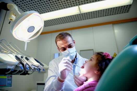 Doctor during visit of female child in dental clinic, dentist checking teeth of young baby girl