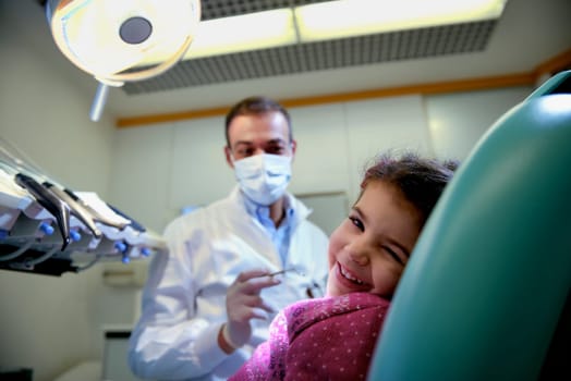 Doctor during visit of female child in dental clinic, portrait of young baby girl looking at camera and smiling