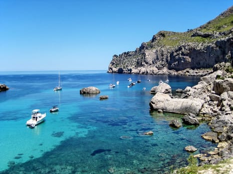 Scenic bay with clear turquoise water, boats, rocks, and mountains