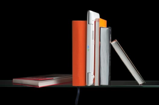 white laptop computer between books on the glass shelf