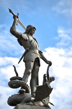 beautiful old statue of knight killing dragon (or snake) with blue cloudy sky in background