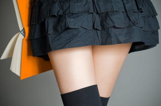 view of the lower body part of woman wearing skirt and stockings holding book in her hands