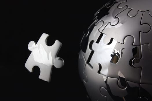 Floating jigsaw peice over chrome puzzle globe
