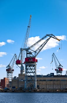 sea port cranes with blue cloudy sky in background and water in foreground in Helsinki port, Finland