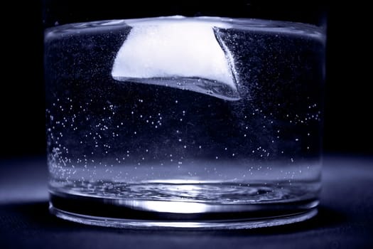 ice floating in the water in the glass with blue tint and black background