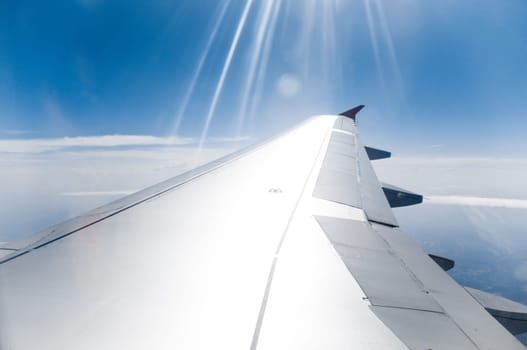 view on blue cloudy sky and earth beneath with sun rays hitting plane wing in foreground