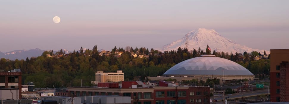 A full moon appears on the horizon near Mt Rainier and the Tacoma Dome