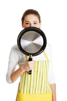 Young smiling caucasian teen girl dressed in apron, smiling behind the frying pan, isolated on white.