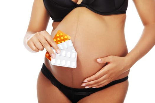 Young beautiful pregnant woman holding pills in front of her belly