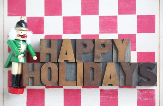 a nutcracker with the words 'happy holidays' in wood type on a stenciled checkerboard