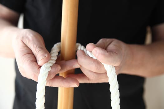 a man begins to tie a thick rope around a wooden pole