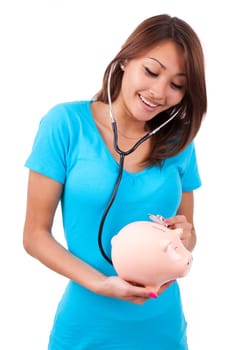 Young happy beautiful asian woman using stethoscope on her piggy bank, isolated on white background - Asian people