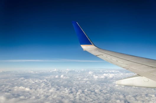 Wing of an airplane with beautiful white clouds and a deep blue sky