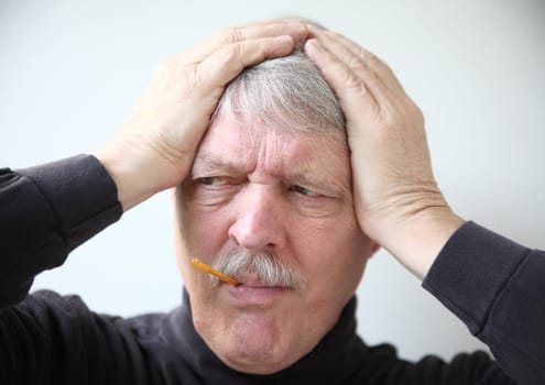 older man holds his head while taking temperature