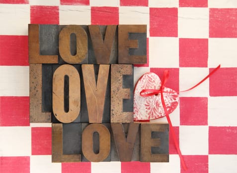 the word love repeated three times with a handmade heart ornament on a checkerboard