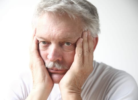 senior man rests his face in his hands and looks disappointed or bored