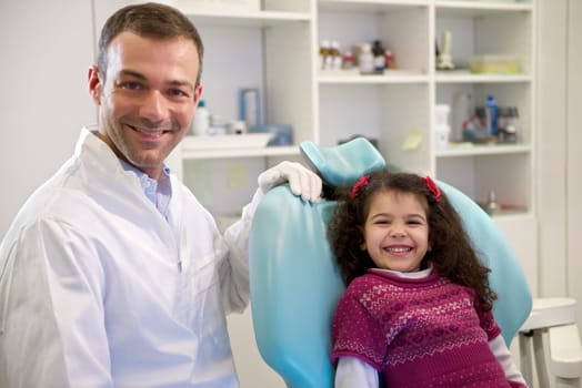 Doctor during visit of female child in dental clinic, portrait of young baby girl looking at camera and smiling