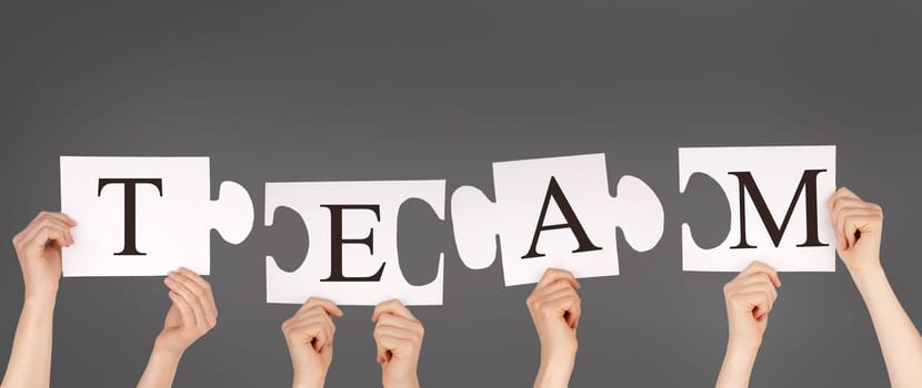 hands holding piecesof a puzzle building the word TEAM, gray background