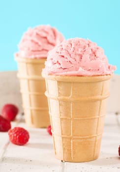 Raspberries ice cream in front of other in waffle on white wood