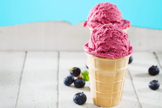 Blueberries ice cream in cone in front of other on white wood