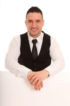 Businessman sitting behind a sign with copy space and has his hands casually over it. He looks friendly into the camera.