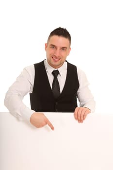 A young man,in a business outfit,points to a white sign and looks friendly into the camera.